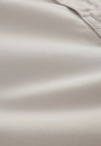 Gros plan sur un tissu lisse beige clair avec une texture de tissage fine visible et une couture surpiquée dans le coin supérieur droit.