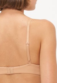 Nude bra with adjustable straps, hook-and-eye closure, smooth fabric, and minimalist design. Features subtle stitching details on the band.