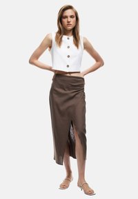 Hvid cropped top med runde knapper, parret med en brun indhyllet midi-nederdel med en sideslids og lyse farvede sandaler med stropper.