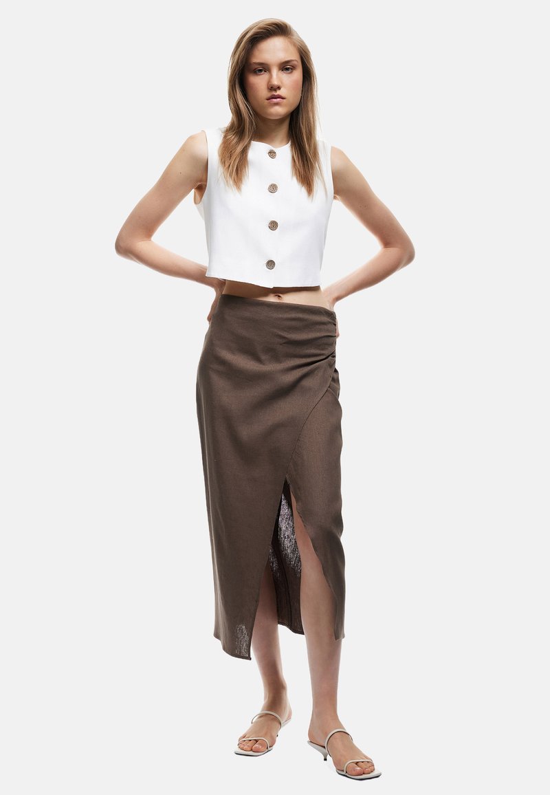 Hvid cropped top med runde knapper, parret med en brun indhyllet midi-nederdel med en sideslids og lyse farvede sandaler med stropper.
