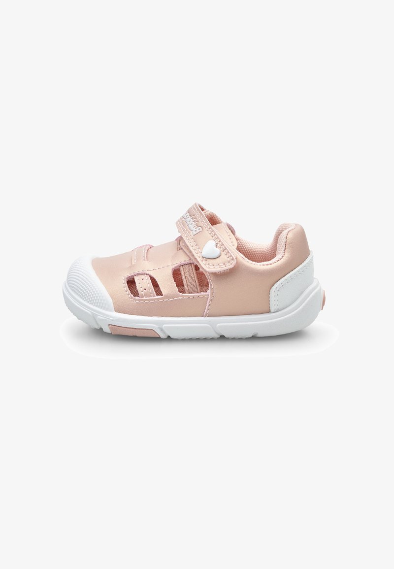Zapatilla deportiva de color rosa claro con diseño recortado, suela y puntera blancas, correa ajustable y un adorno de corazón en la correa.