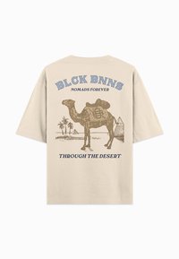 Beige katoenen t-shirt met een kamelenillustratie, palmbomen, piramides en de tekst "BLCK BNNS NOMADS FOREVER" in blauw en donkerblauw.