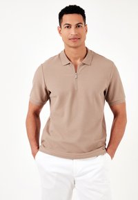 Bēžs polo krekls ar puscibi, īsām piedurknēm un teksturētu audumu. Saskaņots ar baltām biksēm, radot ikdienišķu izskatu.