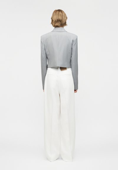 Άτομο με ξανθά κοντά μαλλιά που φοράει ένα κοντό γκρι σακάκι και λευκό παντελόνι με φαρδιές γραμμές και ψηλή μέση, φαίνεται από πίσω.