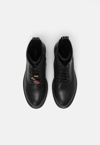 Bottes chevilles en cuir noir à finition lisse, avec lacets, fermetures éclair latérales et accents métalliques décoratifs à l'avant.