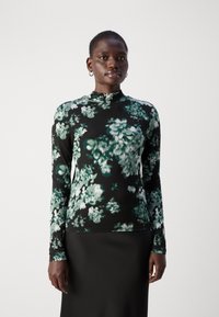 Zwarte langemouwen top met groen bloemenpatroon, voorzien van een hoge halslijn en een gladde textuur, gedragen met een eenvoudige zwarte rok.