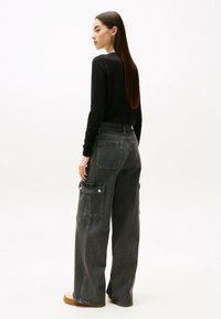 Top negro de manga larga y pantalones cargo de corte holgado en gris carbón con bolsillos laterales. Textura de tela suave con una silueta relajada.