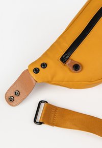 Borsa a tracolla gialla in tessuto con zipper nera, dettagli in pelle marrone e bottoni a pressione. Cinghia regolabile per diverse lunghezze. Superficie texturizzata.