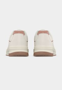 Paire de baskets blanches avec des accents marron clair au talon et aux semelles, vues de dos sur un fond blanc uni.
