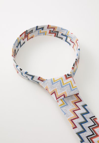 Daudzkrāsains zigzag raksts uz auduma kaklasaites ar pelēku pamatu, ar gludu tekstūru un drošu mezglu šaurākajā galā.