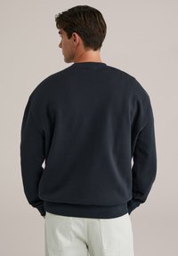 Granatowy sweatshirt z okrągłym dekoltem, opadającymi ramionami oraz ściągaczami na mankietach i dole. Miękka, teksturowana tkanina o luźnym kroju.
