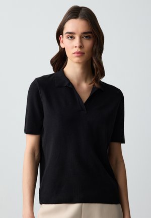 Zwarte polo met korte mouwen in een zachte gebreide stof met een platte kraag, met een relaxed fit en een geribbelde accenta bij de zoom.