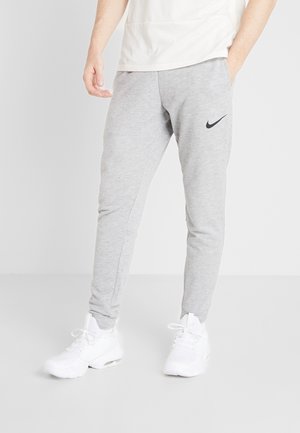 Person trägt hellgraue Nike-Sweathosen und weiße Sneakers, steht mit einer Hand in der Tasche und der anderen entspannt an der Seite.