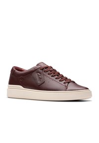 Sneaker in pelle marrone con punta rotonda, lacci tono su tono e suola in gomma beige a contrasto. Presenta una toppa con logo sul lato laterale e dettagli perforati.