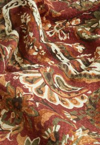 Gros plan d’un tissu à texture froissée présentant un motif floral et cachemire complexe en rouge, orange, vert et blanc.