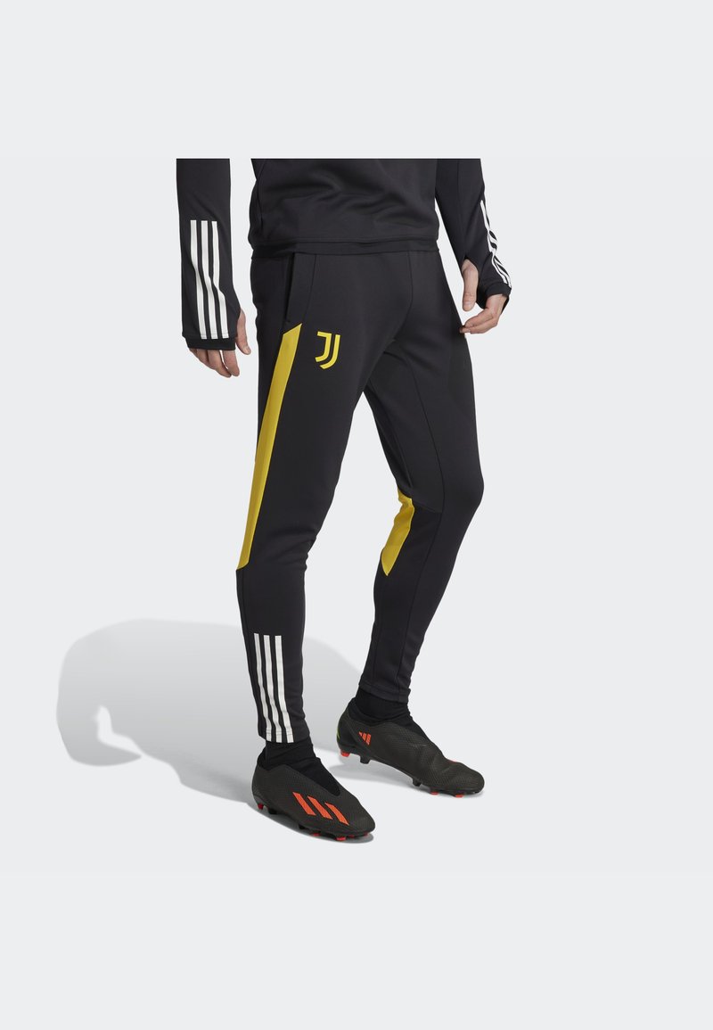 Schwarze Sporthose mit gelben Seitenstreifen und einem Juventus-Logo. Zusätzlicher Weißer Dreistreifen-Design am Bund und an den Ärmeln.
