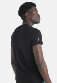 Camiseta negra de manga corta con cuello redondo, hecha de tela suave, que presenta un sutil detalle del logo en el hombro izquierdo.