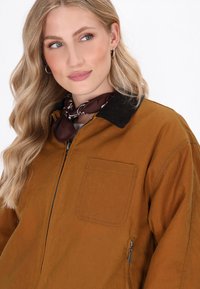 Bruine jas met een rits, een corduroy kraag en een zijzak. Gelaagde stof met een gladde afwerking, met een extra voorzak.
