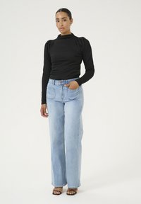 Black long-sleeve top with puffed shoulders paired with light blue wide-leg jeans. The outfit features a high neckline and casual design.