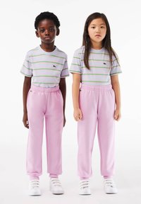 Deux enfants se tiennent côte à côte. Ils portent des t-shirts rayés violet clair et des pantalons de survêtement roses, complétés par des baskets blanches.
