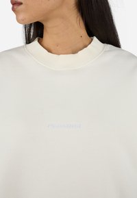Felpa off-white con colletto a costine e tessuto testurizzato. Caratterizzata da un logo "PEGADOR" ricamato in leggero viola.