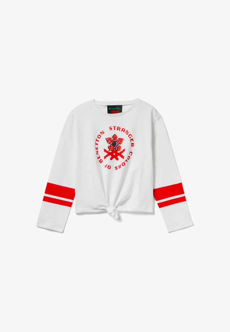 Bílá košile s dlouhým rukávem a červenými pruhy na rukávech, s kulatým červeně černým motivem "Stranger Colors" a uzlovým detailem na lemu.