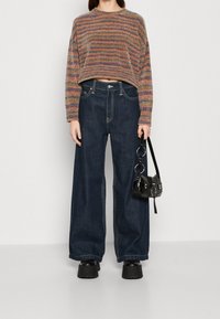 Gehaakte trui met meerkleurige horizontale strepen, gecombineerd met wijde donkere denim jeans. Accessoires zijn een kleine zwarte handtas en platform schoenen.