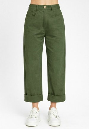 Pantaloni verdi a vita alta e gamba larga con orli risvoltati, bottoni frontali e tasche, indossati con sneaker bianche con lacci.