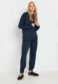 Felpa a coste di colore navy con maniche lunghe, abbinata a pantaloni cargo coordinati dotati di tasche. Sneakers nere con dettagli bianchi completano l'outfit.