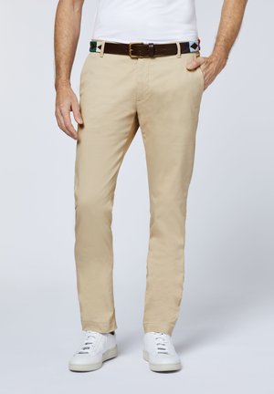 Beige chinos made of cotton, featuring a straight leg design. Paired with a brown leather belt and white sneakers.