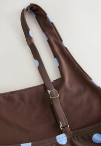 Maillot de bain en tissu marron à pois bleu clair, avec bretelle ajustable et détail boucle en métal.
