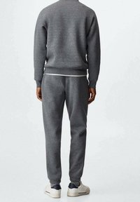 Gråt sweatshirt- og joggingtøjsæt lavet af blødt stof, med ribstrikkede manchetter og en afslappet pasform. Hvid t-shirt synlig under.