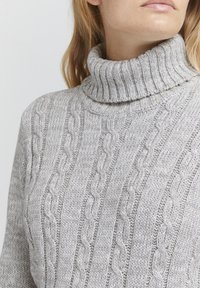 Gray cable-knit turtleneck sweater featuring a ribbed neckline, textured pattern, and a soft, chunky knit design.
