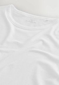 Balta kokvilnas T-krekls ar apaļu kakla izgriezumu un mīkstu tekstūru, ar etiķeti, kas norāda lielumu un izcelsmes valsti.