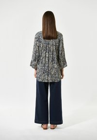 Blusa de manga larga impresa en azul marino y crema con un patrón floral, con detalle de espalda fruncida, combinada con pantalones de pierna ancha oscuros y sandalias planas.