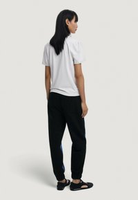 Top blanco de manga corta y joggers negros con rayas laterales azules. Los joggers cuentan con una cintura elástica y tobillos ajustados. Calzado negro.