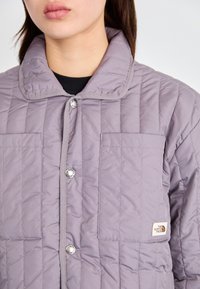 Ροκοκό, μοβ εξωτερικά ρούχα με κλείσιμο με κουμπιά, στρογγυλωτό γιακά και δύο μπροστινές τσέπες. Εκθαμβωτική επωνυμία στην κάτω δεξιά τσέπη.