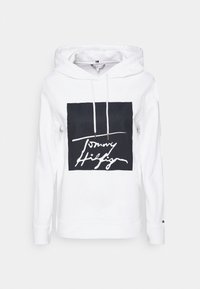 Bílá mikina s kapucí s velkým černým čtvercem, na kterém je bílé písmové logo. Má stahovací kapuci a zpevněné manžety na rukávech.