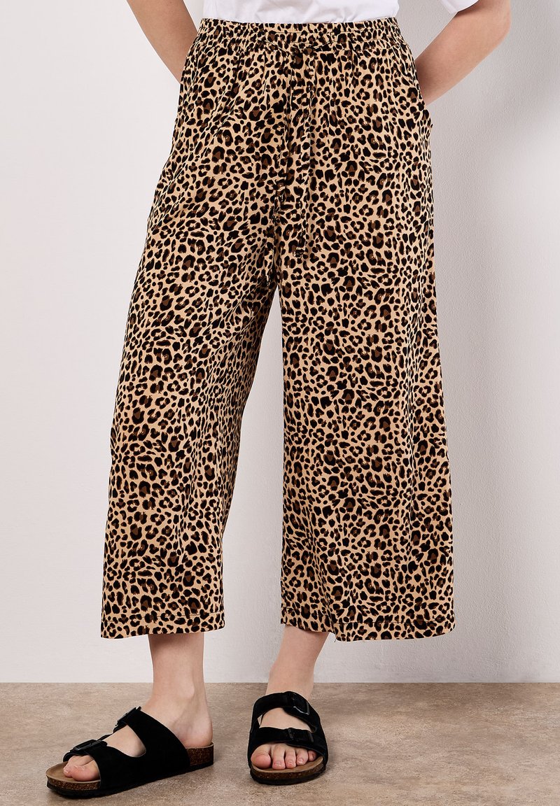 Leopardenmuster-Hose mit weitem Bein, ausgestattet mit einem elastischen Bund, zwei Seitentaschen und aus weichem, leichtem Stoff. Kombiniert mit schwarzen Slidesandalen.