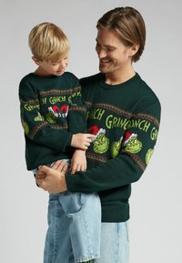 Pulls en maille vert foncé pour adulte et enfant avec un motif Grinch, accents rouges et motifs à thème de fête. Col rond classique, coupe décontractée.