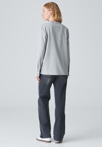 Felpa grigia a maniche lunghe con collo rotondo e polsini abbottonati, abbinata a pantaloni larghi grigio scuro e sneakers bianche. Design semplice.