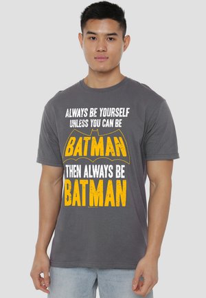 Young man wearing a gray t-shirt with yellow and white text saying "Always be yourself unless you can be Batman then always be Batman."