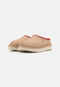 Beige nubukist slip-on sussid punase kudumisega äärega, millel on tekstureeritud tald ja ümar varvas, pakkumaks mugavust ja lihtsat selga panemist.