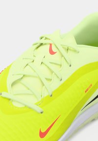 Zbliżenie na neonowożółty but biegowy Nike z jasnopGreenowymi sznurówkami i czerwonymi logo swoosh na języku i boku.
