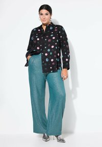 Zwarte blouse met kleurrijke stippen; turquoise wijde broek; glanzende textuur; zilveren hoge hakken. Gestructureerd ontwerp en moderne pasvorm.