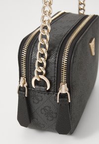 Sac à main noir texturé avec des détails de fermeture éclair dorés, double fermetures éclair et une chaîne en bandoulière. Présente un petit emblème et des accents en cuir.