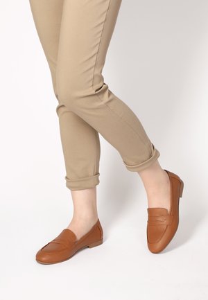 Braune Lederloafers mit einem gestickten Design, niedrigem Absatz und glatter Textur. Kombiniert mit hochgekrempelten beigen Hosen.