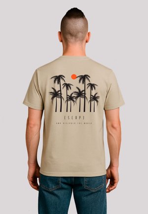 Beige T-Shirt mit schwarzem Palmen-Graphic und orangefarbener Sonne, mit dem Text "ESCAP3 AND DISCOVER THE WORLD" darunter. Kurze Ärmel, aus Baumwolle.