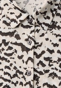 Beige skjorta med knappslå och ett svart abstrakt mönster, med krage, bruna knappar och en liten bröstficka. Mjuk tygkänsla.