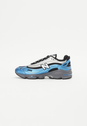 Niebiesko-srebrne buty sportowe New Balance 1000 z czarnymi akcentami i grubą szarą podeszwą, widoczne z boku na białym tle.